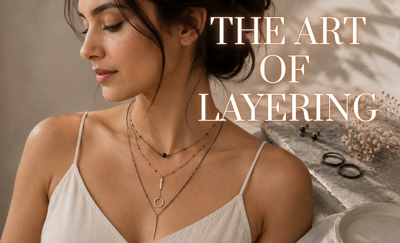 Woman wearing layered lightweight necklaces with delicate pendants and a cream outfit in a minimalist editorial setting, demonstrating effortless necklace layering for everyday style.